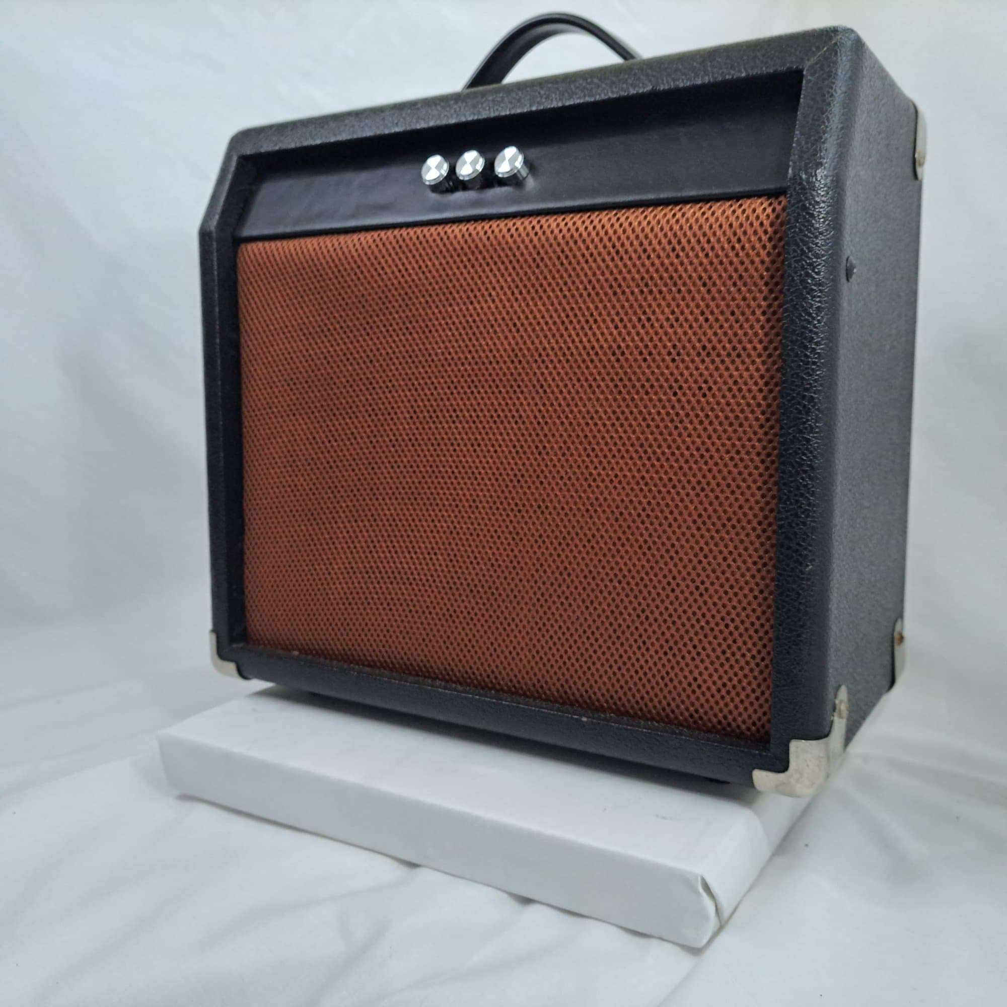 Small amplifier style speaker with a woven cane grille and a carry handle